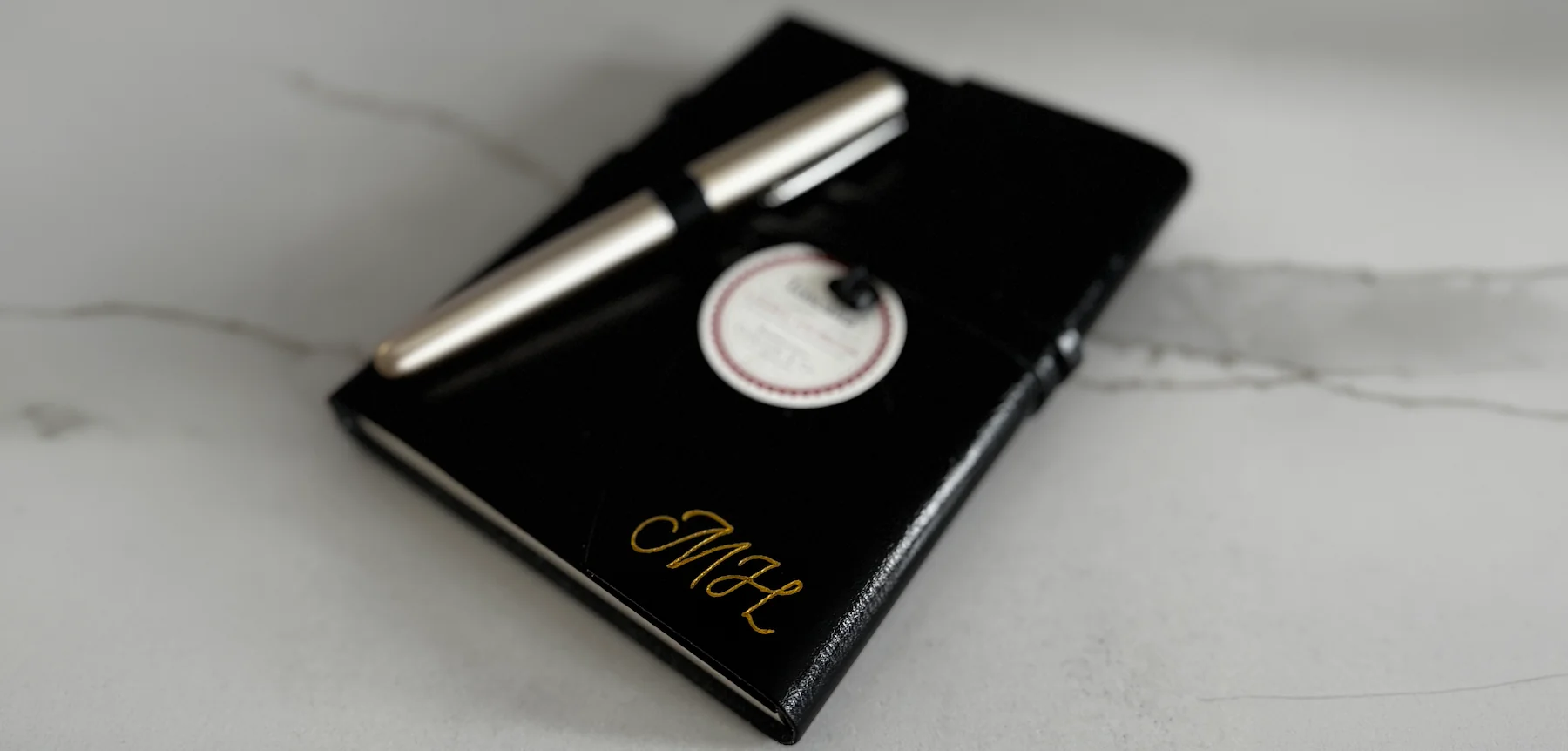 Black keepsake with gold monogram beside a pen